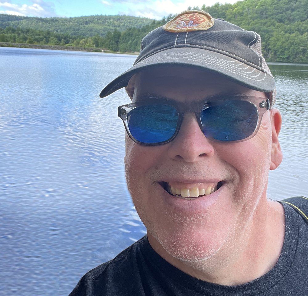 Mike McKillop of Woodwork By Mike, smiling by a lake